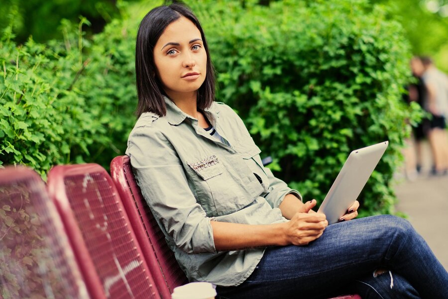 portrait-attractive-brunette-female-sits-bench-holds-tablet-pc-summer-park_613910-14416