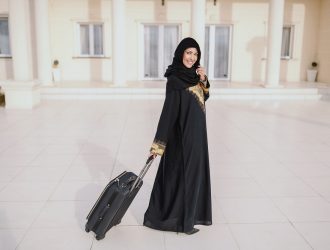 smiling-muslim-woman-traditional-wear-standing-front-her-house-holding-luggage