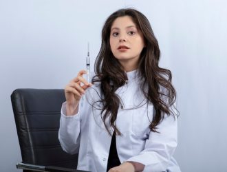 portrait-female-doctor-medical-mask-white-coat-holding-syringe_114579-36798