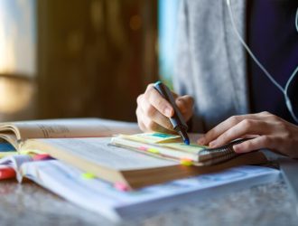 shot-young-male-student-sitting-table-writing-notebook-young-male-student-studying-cafe_217236-342