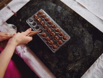 top-view-chocolatier-holding-candy-bag-squeezing-liquid-warm-chocolate-mass-into-candy-molds-process-making-handmade-luxurious-chocolates_328764-2704